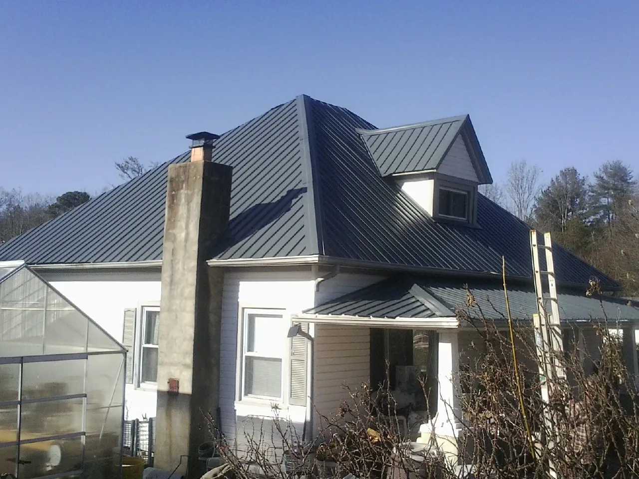 Dark blue standing seam metal roof on a white farmhouse with dormer — Slate & Tile Roof Repair by Roofing Brothers in Lawler