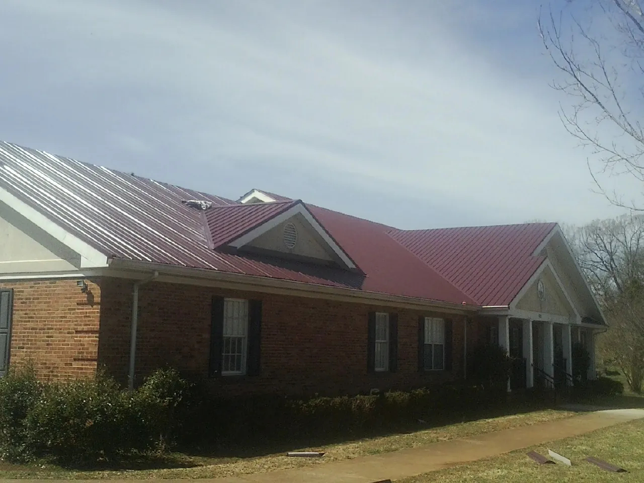 Red metal roof with gabled entries on a long brick building, from a Hail Damage Roof Repair job in Lawler