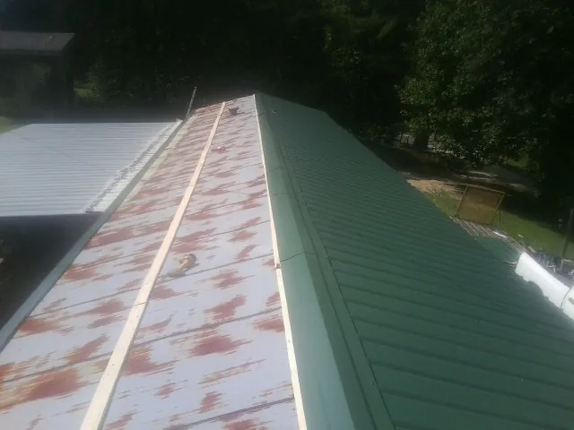 Old rusted panels beside newly installed green metal roofing — Wind Damage Roof Repair by Roofing Brothers in Lawler