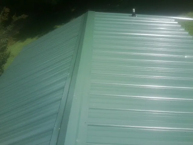 New green metal panels meeting at the ridge of a roof — Flat Roof Repair work by our crew in Lawler