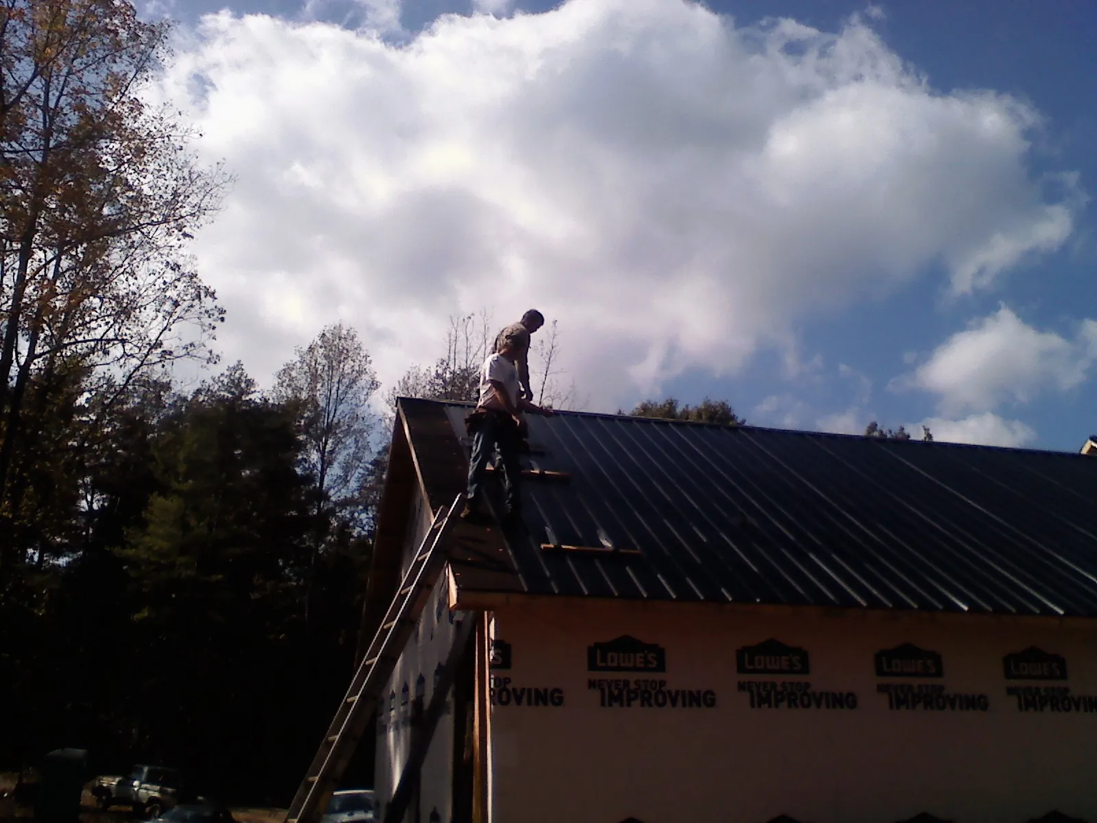Roofer fastening dark metal panels high against a cloudy sky, from a Roof Inspection job in Lawler