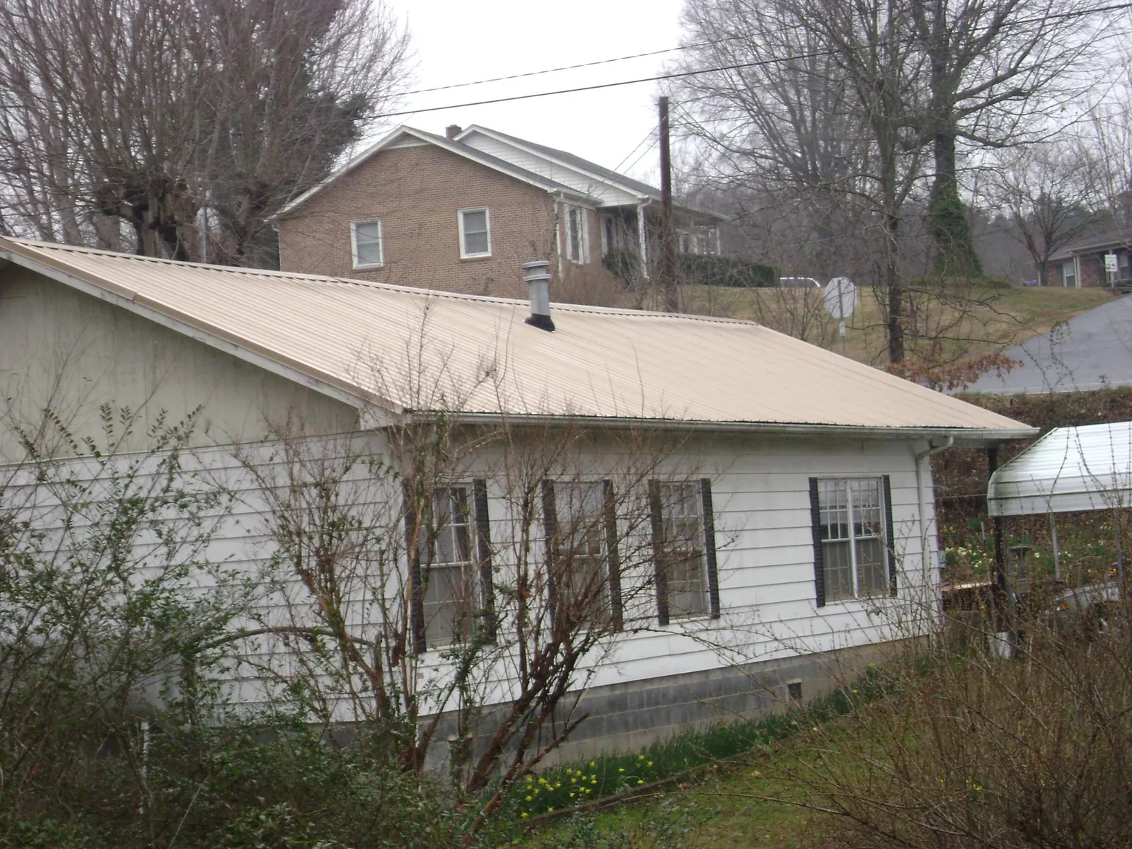 Tan metal roof on a white sided house set into a hillside — Commercial Roofing by Roofing Brothers in Lawler